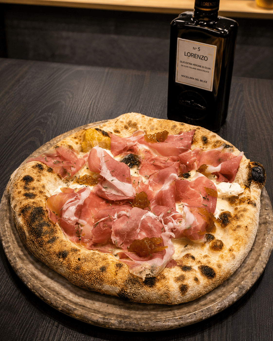 Pizza con prosciutto crudo appena sfornata accanto a una bottiglia di olio extravergine di oliva